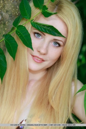 Блондинка в бикини сексуально позируют на фоне зеленых листьев, она эротично выставляет обнаженную пизду и груди